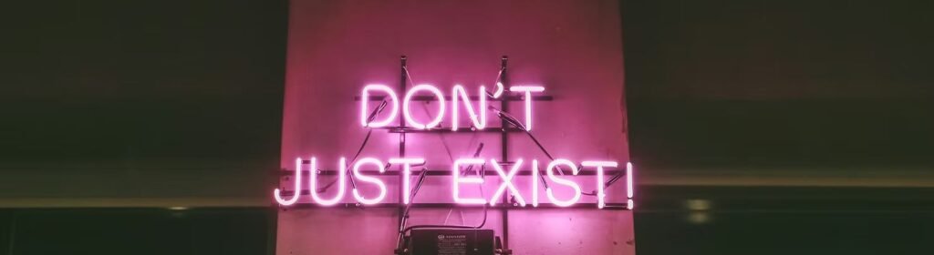 A pink neon sign reading Don't just exist