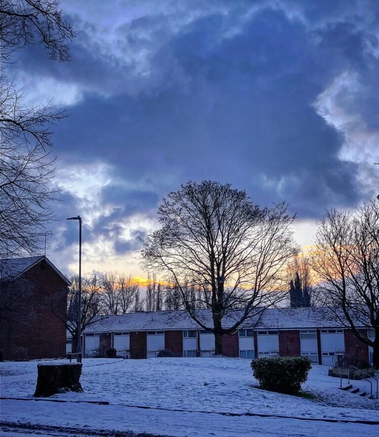 Snow on the ground beside a row of houses under a break in the clouds